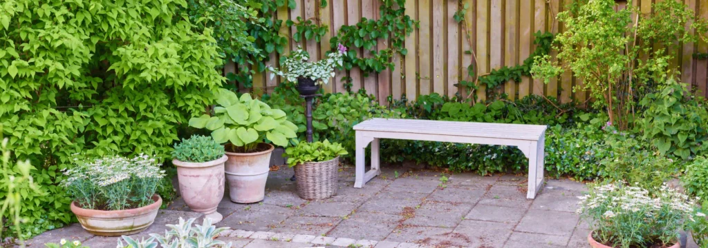 ein  schöner grüner Garten mit einer Holzbank und Topfpflanzen im Hinterhof